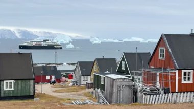 Grönland 'ın kayalık kıyı şeridi boyunca renkli evler bulunur. Buzdağları, parlak bir günde kutup manzarasının dingin güzelliğini gözler önüne seren sularda görülebilir..