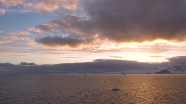 Güneş dağların ardında batarken güzel bir günbatımı, turuncu ve mor tonlarıyla gökyüzünü boyar. Sakin sular bu huzurlu deniz manzarasındaki çarpıcı renkleri yansıtıyor..