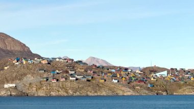Grönland kıyılarında canlı bir yerleşim yeri keşfetmek, kayalık tepeler ve sakin sulara karşı renkli evler. Bu pitoresk konum çarpıcı görüntüler sunar.