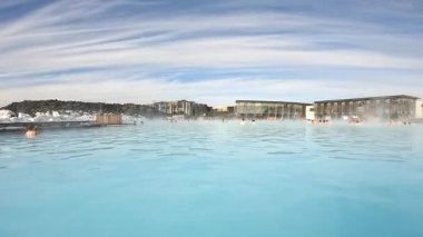 İnsanlar İzlanda 'daki bir jeotermal kaplıcada mineral zengini sularda yüzmeyi seviyor. Güneş batıyor, sudan yükselen buharın üzerine güzel bir parıltı saçıyor..