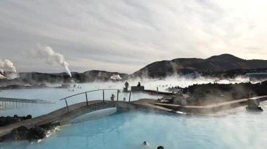 İnsanlar İzlanda 'daki bir jeotermal kaplıcada mineral zengini sularda yüzmeyi seviyor. Güneş batıyor, sudan yükselen buharın üzerine güzel bir parıltı saçıyor..