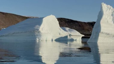 Kuzey Kutbu 'ndaki sakin suların üzerinde sersemletici bir buzdağı kuleleri, sakin denizdeki etkileyici şeklini yansıtıyor. Parlak güneş ışığı sahneyi aydınlatır, buzun dokusunu geliştirir..
