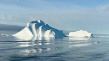 Kuzey Kutbu 'ndaki sakin suların üzerinde sersemletici bir buzdağı kuleleri, sakin denizdeki etkileyici şeklini yansıtıyor. Parlak güneş ışığı sahneyi aydınlatır, buzun dokusunu geliştirir..