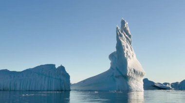 Kuzey Kutbu 'ndaki sakin suların üzerinde sersemletici bir buzdağı kuleleri, sakin denizdeki etkileyici şeklini yansıtıyor. Parlak güneş ışığı sahneyi aydınlatır, buzun dokusunu geliştirir..