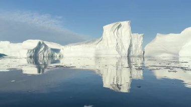 Kuzey Kutbu 'ndaki sakin suların üzerinde sersemletici bir buzdağı kuleleri, sakin denizdeki etkileyici şeklini yansıtıyor. Parlak güneş ışığı sahneyi aydınlatır, buzun dokusunu geliştirir..