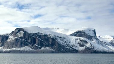 Nefes kesici uçurumlar bir yaz günü sakin suların üzerinde görkemli bir şekilde yükselir. Berrak gökyüzü, kar kaplı zirveleriyle Kuzey Kutbu 'nun güzelliğini sergiliyor..