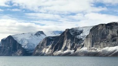 Nefes kesici uçurumlar bir yaz günü sakin suların üzerinde görkemli bir şekilde yükselir. Berrak gökyüzü, kar kaplı zirveleriyle Kuzey Kutbu 'nun güzelliğini sergiliyor..