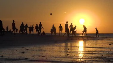 İnsanlar gün batımında voleybol oynamak için plajda toplanıyorlar. Oyuncuların siluetleri parlak gökyüzüne karşı görünür. Günün sıcaklığı eğlence ve kahkahalarla sona erer..