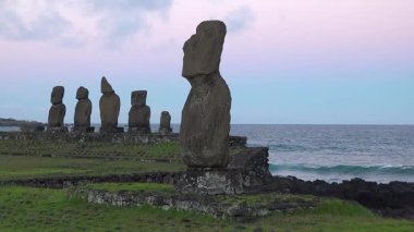 Ziyaretçiler Paskalya Adası 'ndaki ünlü moai heykellerini inceliyorlar. Büyük taş figürler mavi gökyüzüne karşı dik dururlar. Site, öğrenmek ve fotoğraf çekmek için gelen pek çok kişiyi çekiyor..