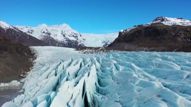 Büyük buz akıntıları İzlanda 'da bir buzulun tabanında hareket eder. Buzun üzerinde parlak güneş ışığı parlıyor. Gökyüzü bazı bulutlarla mavidir. Sahne, doğa ve buz manzarasının güzelliğini gösteriyor..