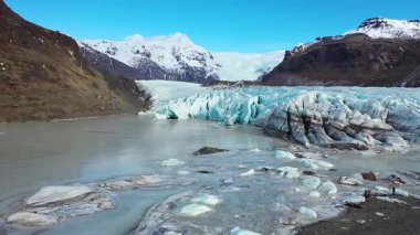 Büyük buz akıntıları İzlanda 'da bir buzulun tabanında hareket eder. Buzun üzerinde parlak güneş ışığı parlıyor. Gökyüzü bazı bulutlarla mavidir. Sahne, doğa ve buz manzarasının güzelliğini gösteriyor..