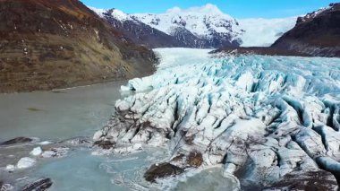 Büyük buz akıntıları İzlanda 'da bir buzulun tabanında hareket eder. Buzun üzerinde parlak güneş ışığı parlıyor. Gökyüzü bazı bulutlarla mavidir. Sahne, doğa ve buz manzarasının güzelliğini gösteriyor..