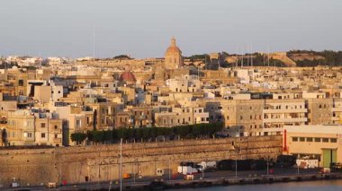 Sudan Vallettas 'ın tarihi binalarının net bir görüntüsü. Güneş parlıyor, kıyı şeridi boyunca duvarları ve tekneleri aydınlatıyor. İnsanlar gün içinde bu bölgeden zevk alıyorlar..