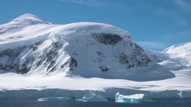 Buzdağları, arka planda duran yüksek dağlar gibi buzlu sularda sürükleniyor. Gökyüzü bulutlu ve manzara soğuk bir günde Antarktika 'nın güzelliğini gösteriyor..