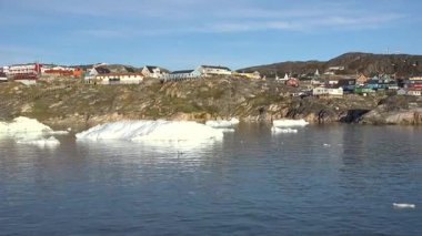 Grönland 'da kıyı boyunca renkli evleri olan küçük bir Arktik köyü. Buzdağları suda yüzer ve manzara doğal güzellikleri gösterir..