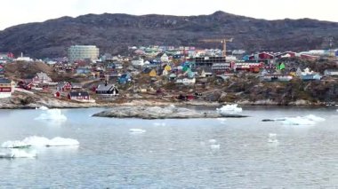 Grönland 'da kıyı boyunca renkli evleri olan küçük bir Arktik köyü. Buzdağları suda yüzer ve manzara doğal güzellikleri gösterir..