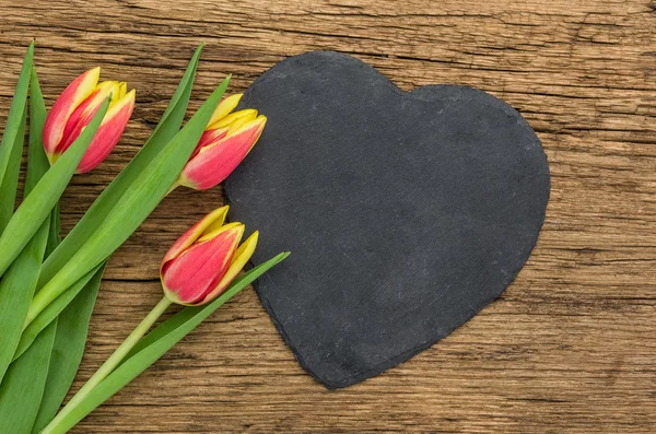 Красные тюльпаны на деревянном фоне с вывеской в форме сердца — стоковое фото