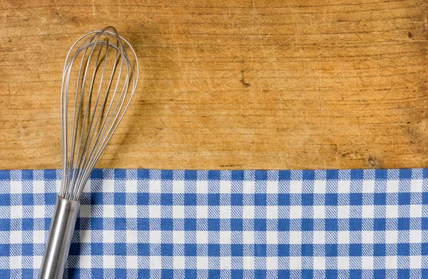 Whisk on wooden background with a blue checkered tablecloth — Stock Photo, Image
