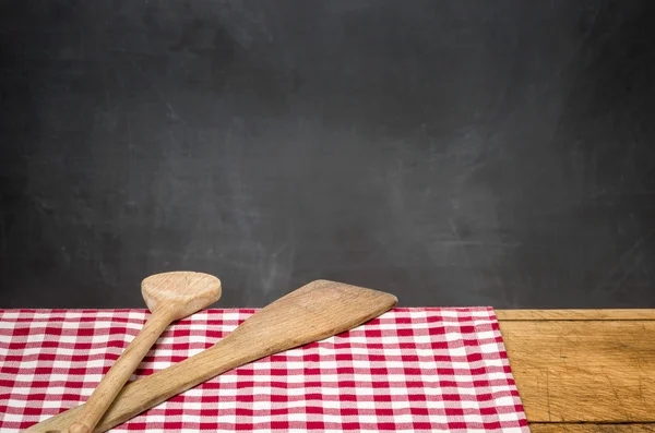 Wooden spoons on a checkered tablecloth in front of a blackboard — Stock Photo, Image