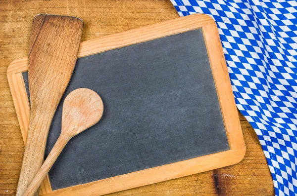 Wooden spoons and chalkboard with a bavarian tablecloth — Stock Photo, Image