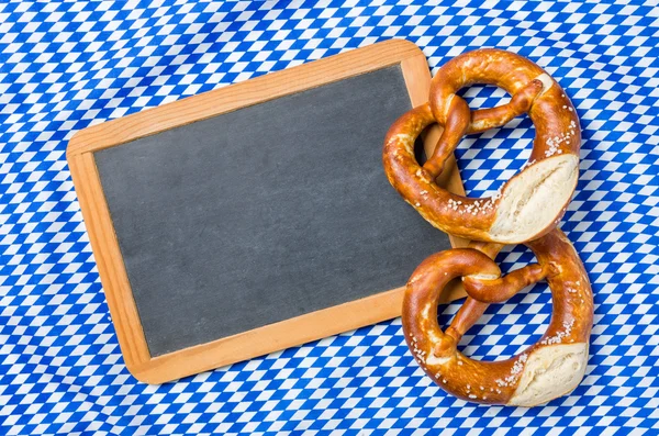 Empty blackboard with pretzels on a bavarian diamond pattern — Stock Photo, Image