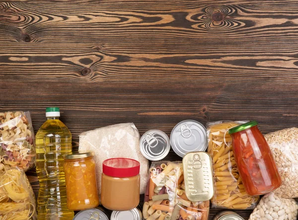 Makarna, pirinç, yağ, fıstık ezmesi, konserve yiyecek, reçel ve diğer bağışları kahverengi ahşap masaya, fotokopi alanının üst görüntüsü