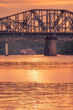 Cincinnati, OH - 18 Ağustos 2018; nehir teknesi günbatımında Ohio nehri üzerindeki çelik köprünün altından geçer.
