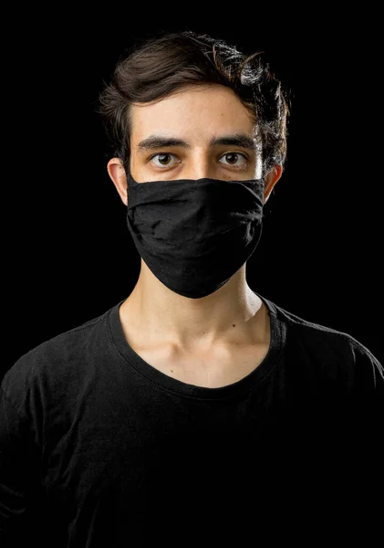 Young man wearing black face mask. Pandemic coronavirus covid-19 quarantine period concept. Black background studio.