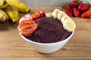 Acai, elinde Brezilya dondurması kasesi olan bir kadın. Ahşap arka planda meyveler. Yaz menüsü ön görünümü