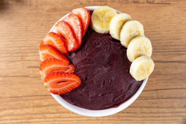 Acai, elinde Brezilya dondurması kasesi olan bir kadın. Ahşap arka planda meyveler. Yaz menüsü ön görünümü