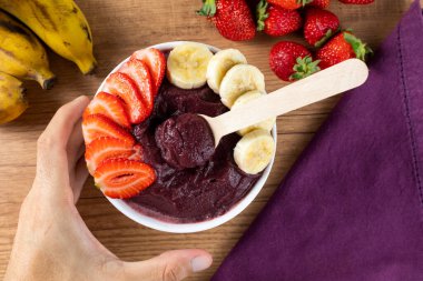 Acai, elinde Brezilya dondurması kasesi olan bir kadın. Ahşap arka planda meyveler. Yaz menüsü ön görünümü