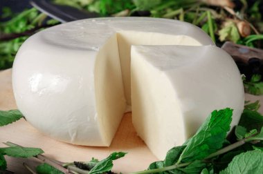 Ahşap bir tahtanın üzerinde yeşil otlarla kaplı bir peynir. Gürcistan peyniri sulguni 