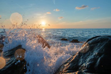 Deniz dalgaları, günbatımının güzel arka planıyla büyük kayaların üzerinde eziliyor.