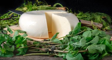 Ahşap bir tahtanın üzerinde yeşil otlarla kaplı bir peynir. Gürcistan peyniri sulguni 