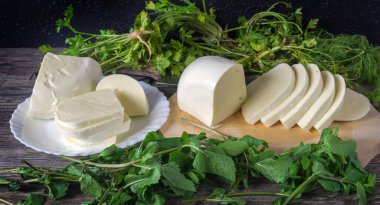 Ahşap bir masada dilimlenmiş peynir ve yeşil otlar. Gürcistan peyniri sulguni