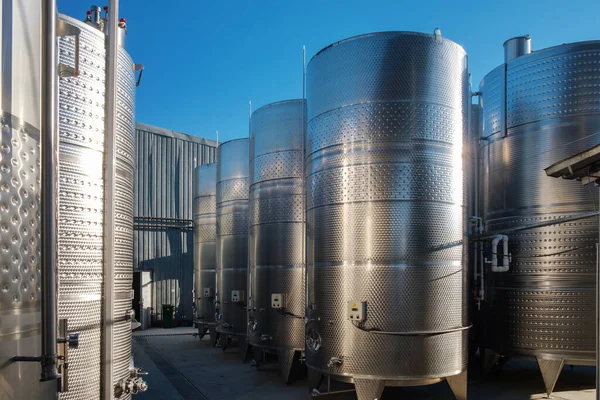 Stainless tanks for processing and fermentation wine production in the open air with blue sky background. Modern wine factory