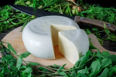 Ahşap bir tahtanın üzerinde yeşil otlarla kaplı bir peynir. Gürcistan peyniri sulguni 