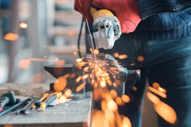 Üzerinde kıvılcımlar uçuşan bir metal üzerinde dairesel bir değirmenle çalışan işçiler, seçici bir odak noktası.