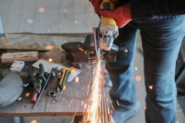 Üzerinde kıvılcımlar uçuşan bir metal üzerinde dairesel bir değirmenle çalışan işçiler, seçici bir odak noktası.