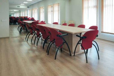 Konferans odasının içinde büyük aynalar, etrafında kırmızı sandalyeler olan büyük bir masa.