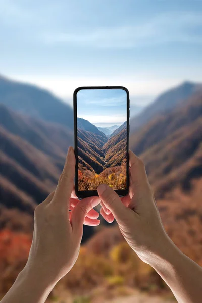 Hands holding tablet and taking photo of a autumn mountains landscape