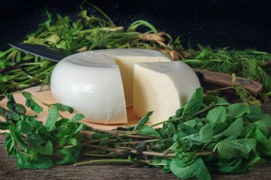 Ahşap bir tahtanın üzerinde yeşil otlarla kaplı bir peynir. Gürcistan peyniri sulguni
