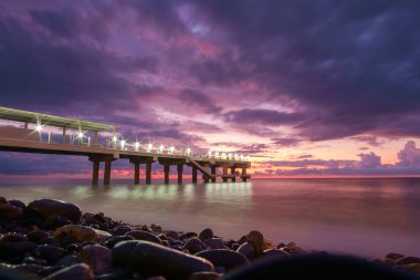 Renkli gün batımı gökyüzü arka plan ile kayalık plajda Işıklı iskele  