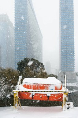 Karla kaplı kapalı cankurtaran botu göl kenarındaki fırlatma sistemine monte edilmiş, gökdelenlerin arka planı...