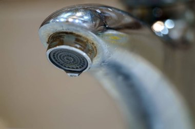 Paslı oluğundan su damlayan bir krom musluğu görüyor. seçici odak