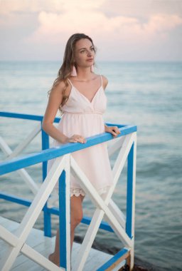 Gün batımı sahilinde genç, zayıf, güzel bir kadın.