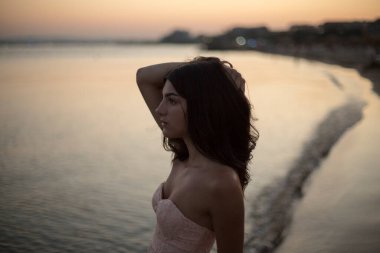 Gün batımı sahilinde genç, zayıf, güzel bir kadın.