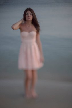 Gün batımı sahilinde genç, zayıf, güzel bir kadın.