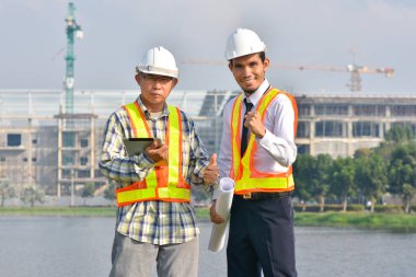 İnşaat alanında ayakta duran iki mühendis mutlu bir başarı, elinde tablet ve plan tutan iki işçi.