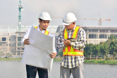 İki Mühendis planlarını elinde tutarak tartışmalı gayrimenkul projesini konuşuyor.